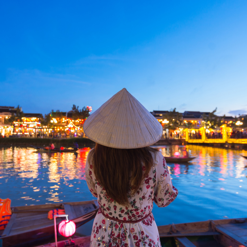 woman looking at the illuminated buildings at thu bon riverside in hoi an vietnam