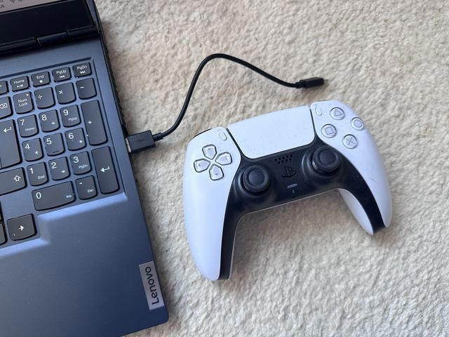 A PS5 DualSense controller next to a laptop and USB-C cable.