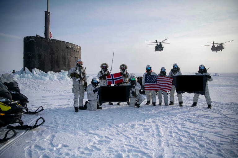 SEALs and Norwegian Naval Special Operations Commandos are pictured next to the Los Angeles-class attack submarine USS Hampton (SSN 767) while two MH-47G Chinook helicopters, assigned to the 160th Special Operations Aviation Regiment (Airborne), hover overhead during an joint submarine/special operations forces integration exercise. Lt.j.g. Martin Carey