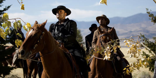 Chief and Decker ride horses through the fields in Outlaw Posse