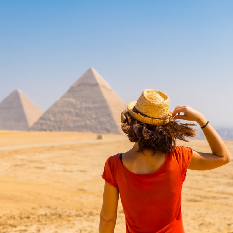 woman in red top looking at pyramids in the distance in egypt