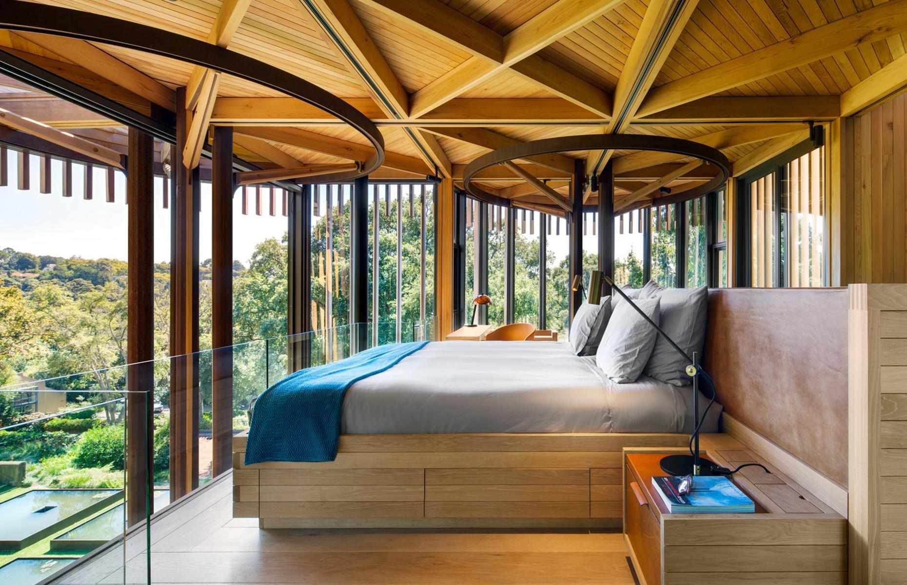 <p>Enclosed by a glass balustrade, the master bedroom can be found on a snug mezzanine level above the main living zone. Designed to double as a lookout platform, the suite boasts stunning vistas across the exterior landscape.</p>  <p>The bed frame and side table were cleverly built into the wall, creating a minimal, seamless finish that makes the most of every inch of space, while a compact but practical en suite bathroom is tucked away in a nook behind the bed.</p>