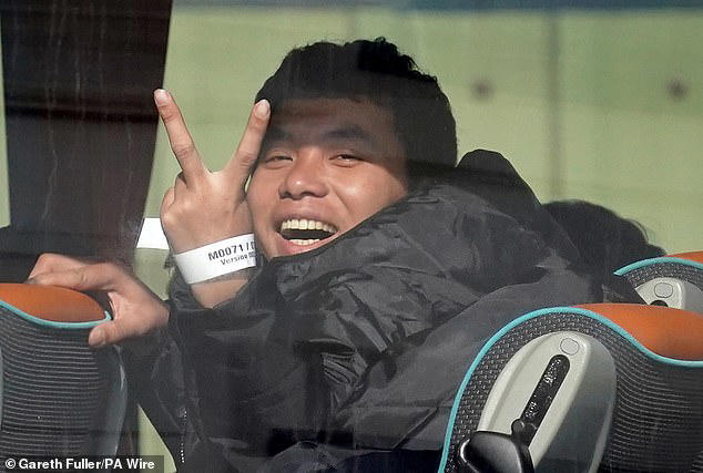 A migrant stuck two fingers up to a camera while sitting on a coach after arriving at Dover today