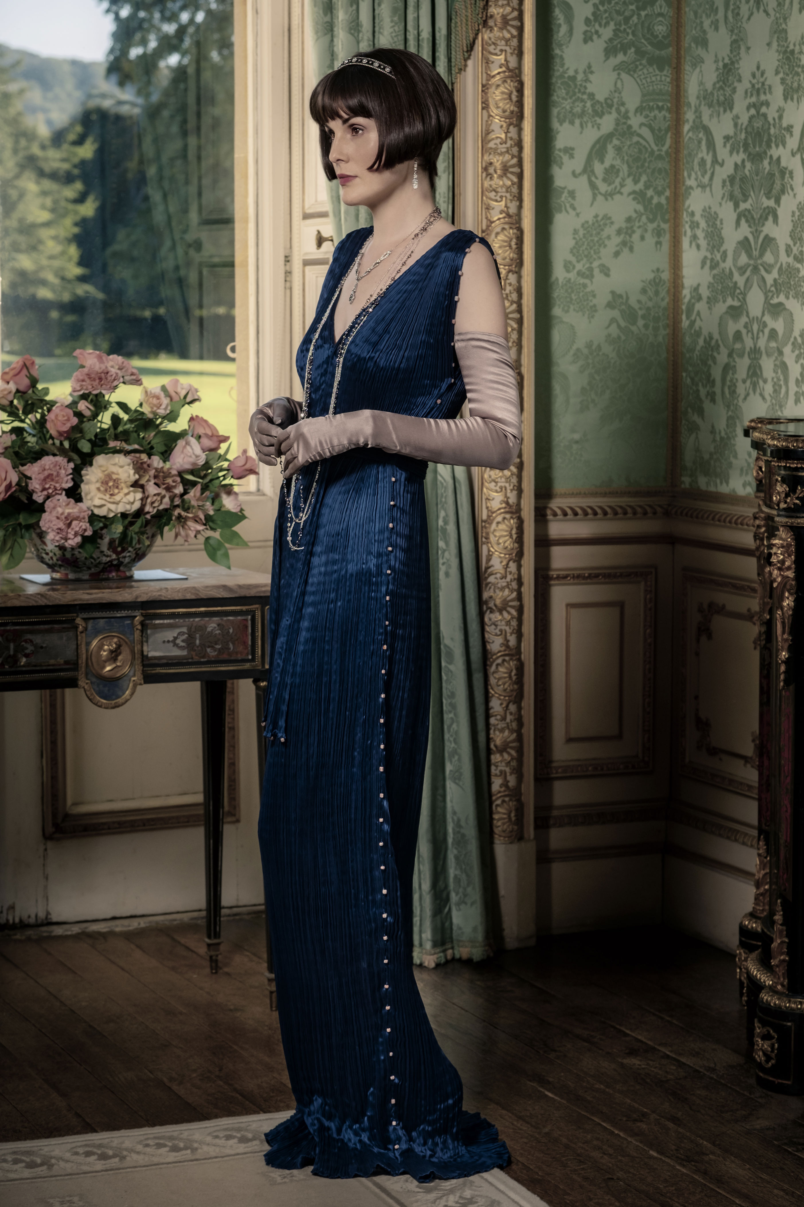 <p><span>For a royal luncheon at Downton Abbey in the 2019 film, Lady Mary donned costume designer Anna Mary Scott Robbins' version of a Fortuny Delphos gown. "I first worked with the legendary textile house Fortuny @fortunyvenezia on the final series of Downton Abbey and this led to a collaboration with them to create a bespoke pleated gown for Lady Mary," Anna wrote on Instagram alongside a </span><a href="https://www.instagram.com/p/B1uB_pegtA3/">sketch</a><span> of the look. "This unique dress is neither vintage nor a replica -- it is a 'new' original, having unlocked the famous and secret pleating technique developed by Mariano Fortuny and his wife and muse, Henriette, and is entirely hand sewn. The silk was dyed to a brilliant, rich Prussian blue that becomes glossier and more luminous after pleating."</span></p>