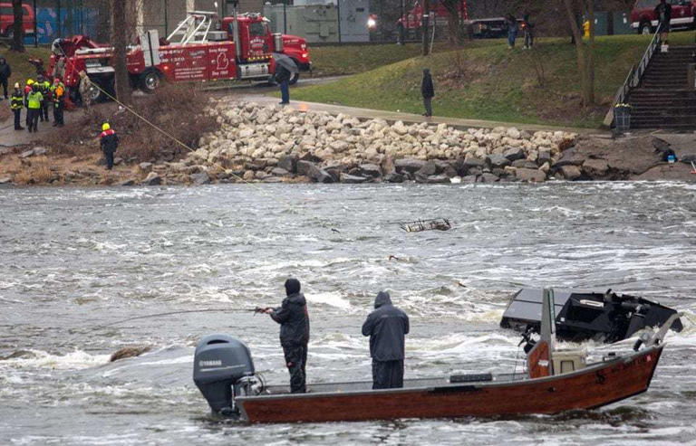 Fishers continue to look for their catch of the day while first responders recover a capsized boat in the Grand River near 6th Street Dam in Grand Rapids, Mich. on Friday, March 8, 2024. The three occupants of the capsized boat were rescued. 2 victims were taken to the hospital for futher evaluation.