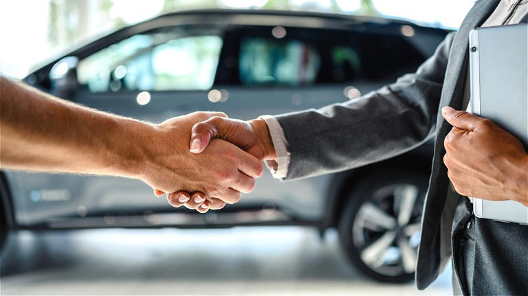 People shaking hands over car