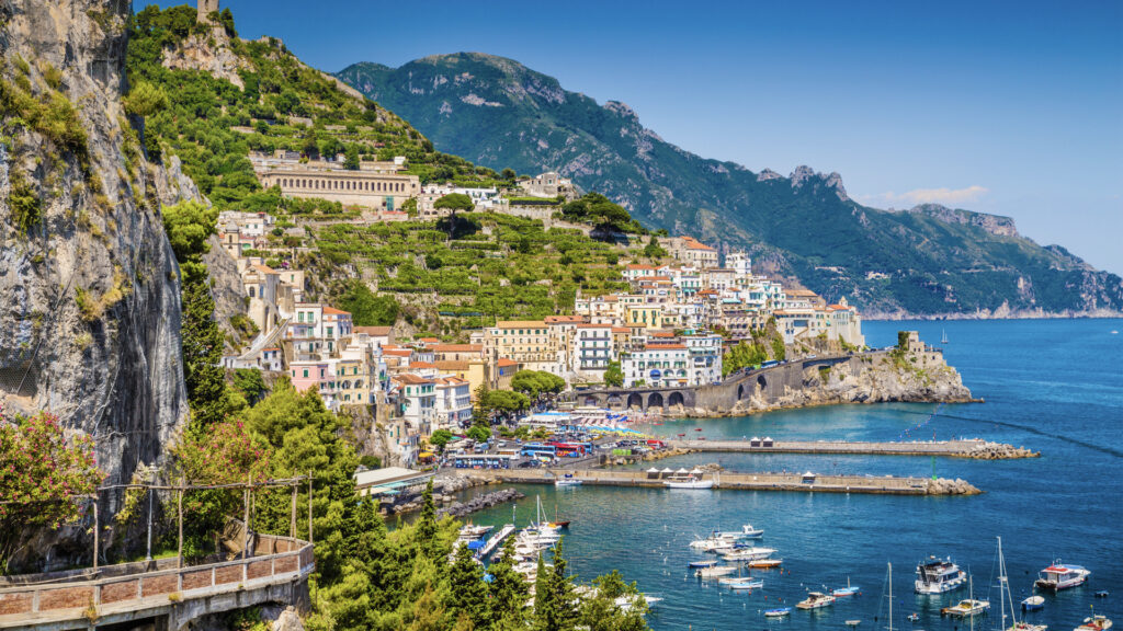 <p>Italy’s famed Amalfi Coast attracts with its dramatic scenery: rugged coastal mountains meet the azure sea in a breathtaking vertical landscape adorned with sun-kissed villages and majestic cliffs. While Cinque Terre and Costa Viola vie for coastal beauty, the Amalfi Coast has enchanted countless luminaries, earning its reputation as a haven for romance. </p><p>From Tennessee Williams to Jackie Kennedy, those captivated by its charms are countless. However, navigating its renowned road can be daunting due to heavy traffic and limited parking. Opting for ferries or public transport offers a more serene exploration of this iconic coastline’s splendor.</p>