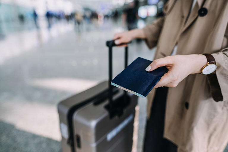 Cropped shot, mid-section of young woman carrying suitcase and holding passport at airport terminal. Ready to travel. Travel and vacation concept. Business person on business trip