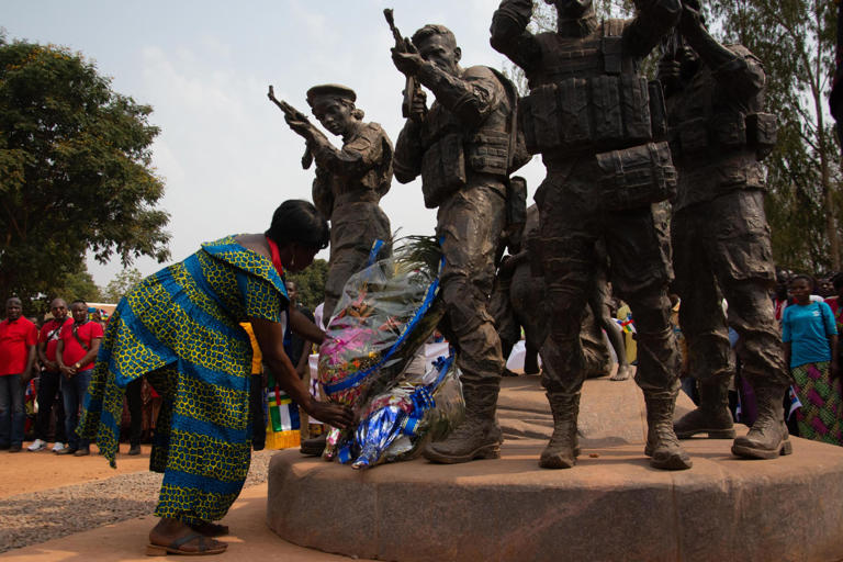 Une femme dépose une gerbe de fleurs au pied d'un monument qui représente des soldats centrafricains et des soldats russes protégeant une femme et ses enfants, à Bangui, en République Centrafricaine.