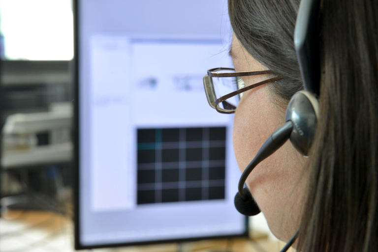 Tight portrait of a young woman with glasses, viewed from behind, with a headset and microphone in front of her computer screen. (Photo by: Andia/Universal Images Group via Getty Images)