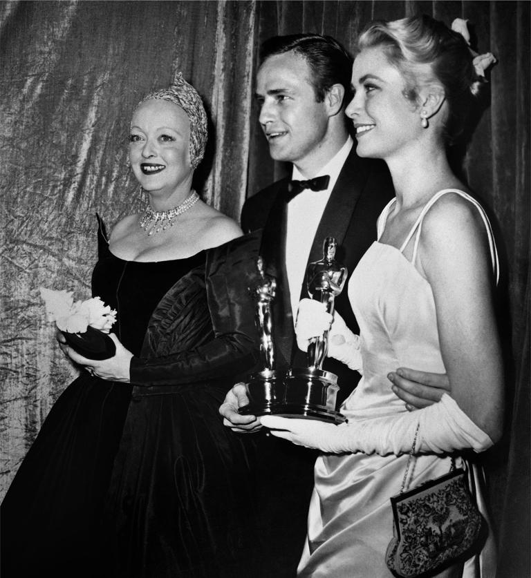 LOS ANGELES - MARCH 30: Actress Bette Davis stands next to winners holding their Oscars, Marlon Brando and Grace Kelly, at the Academy Awards ceremony on March 30, 1955 in Los Angeles, California. (Photo by Frank Worth, Courtesy of Emage International/Getty Images)