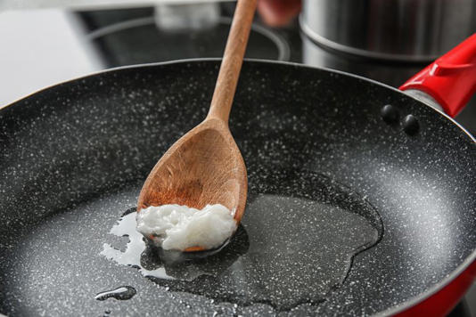 Wooden spoon with coconut oil in frying pan. Healthy cooking