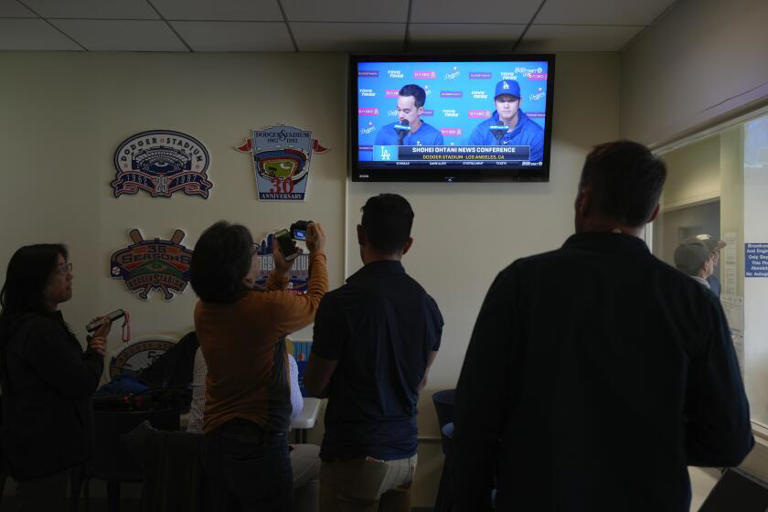 Reporters watch the TV showing Dodgers star Shohei Ohtani, right, and his new interpreter, Will Ireton, during a March 25 news conference in which Ohtani said he "never bet on baseball or any other sports, or have never asked somebody to do on my behalf." ((Jae C. Hong / Associated Press))