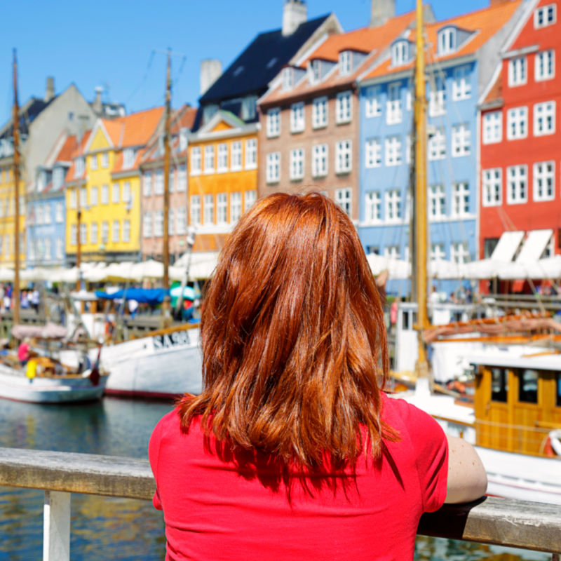 Woman enjoying the scenic view of Nyhavn pier. Colorful building facades with boats and yachts in the Old Town of Copenhagen, Denmark copy