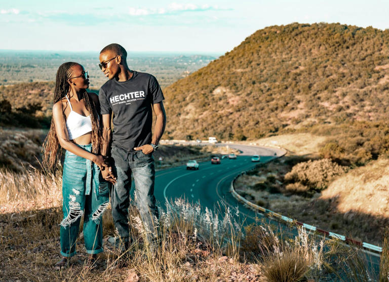 Check out these interactive questions for couples that want to have a forever travel buddy. These are important road trip questions for couples. pictures: a Black couple happily taking a photo in front of a picturesque main rain seemingly on vacation together