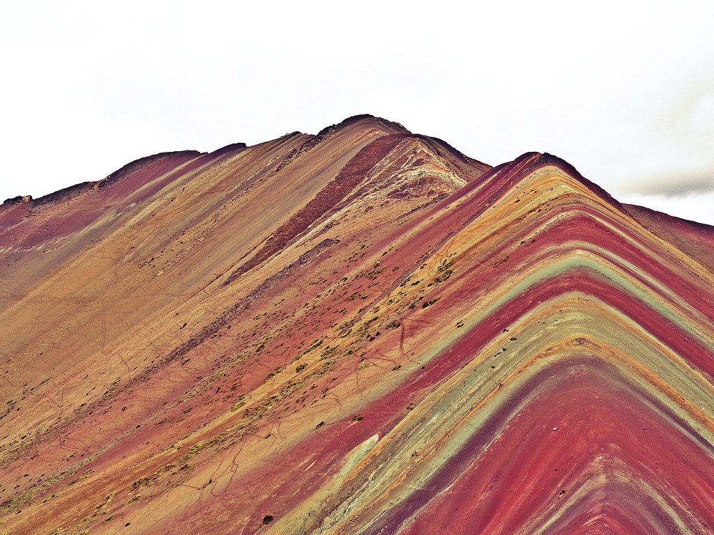 The Rainbow Mountain's striking colors are the result of mineral deposits that have accumulated over millions of years. Layers of iron oxide, copper sulfate, and other minerals have combined to create a painting-like effect on the mountainside, with hues of red, yellow, purple, and green beautifully striping its slopes. This phenomenon occurs due to the sedimentary layers exposed by erosion, which reveals a rainbow effect on the mountain's surface.