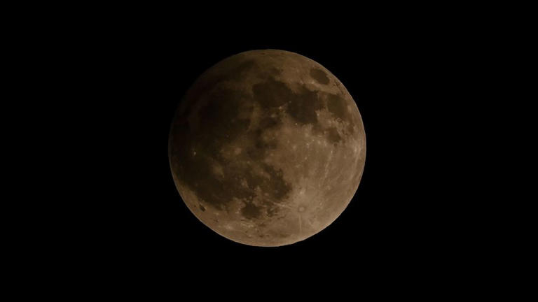 The moon looks slightly darker during a 2023 penumbral lunar eclipse in Banda Aceh, Indonesia. On Monday, the lunar event will begin at 12:53 a.m. ET. - Chaideer Mahyuddin/AFP/Getty Images