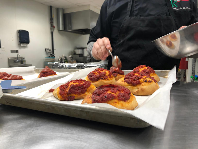 Chef Alessandro De Luca spoons sauce onto pizzette, individual finger food-style pizzas, in his kitchen on Wednesday, March 20, 2024.