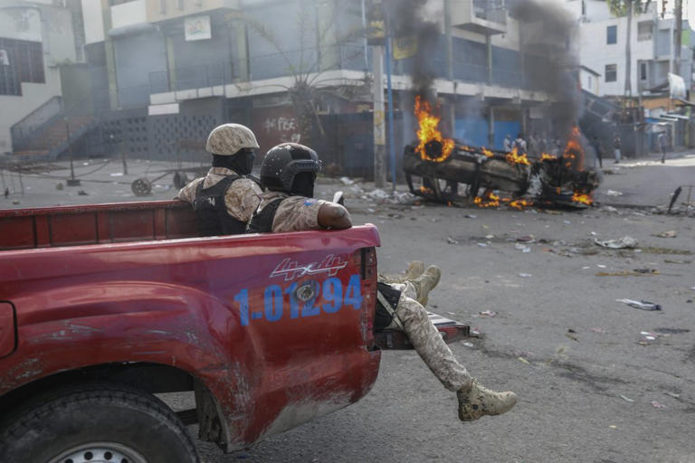 FILE - National police officers ride past a vehicle set on fire in Port-au-Prince, Haiti by protesters on Feb. 7 during a demonstration. Canadian Foreign Minister Melanie Joly told reporters in Ottawa that Global Affairs Canada is now evacuating Canadians from Haiti.