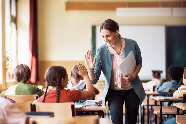 Happy elementary school teacher giving high-five to her student