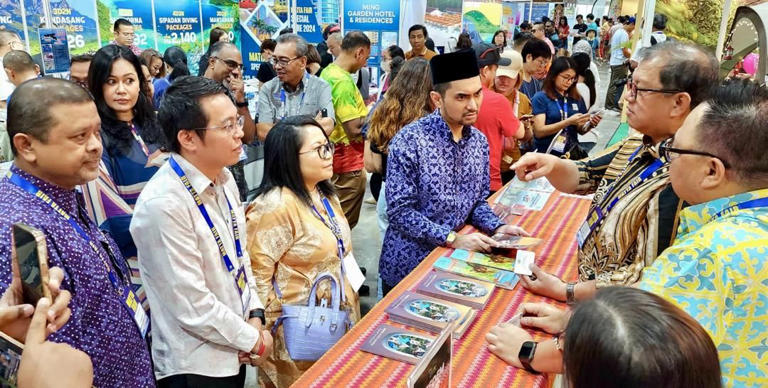 Khairul (third from right, wearing songkok) and federal tourism officials visit the Sabah Tourism Board booth, with Bangkuai (second right) briefing on offerings.