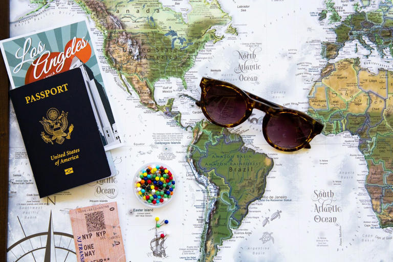 75 travel trivia questions about places around the world. Pictured: a world map with sunglasses, a passport and pins on it.