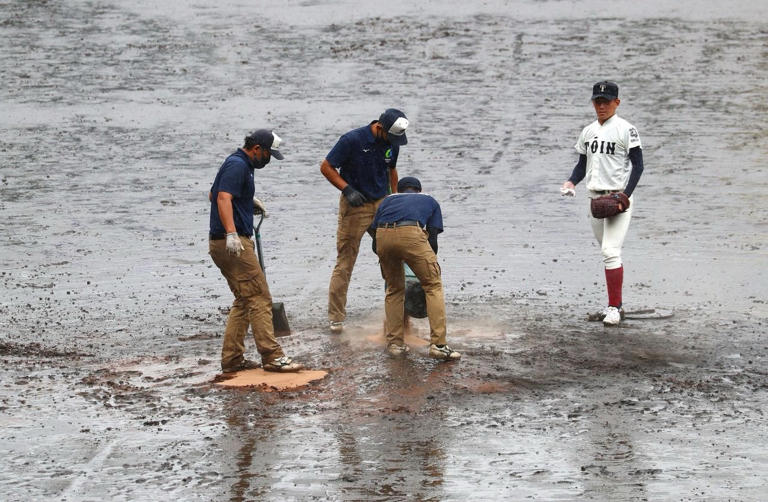 阪神園藝的工作人員正在雨中整備球場，而大阪桐蔭高校的投手竹中勇登則在旁觀察（2021 年 8 月 17 日）