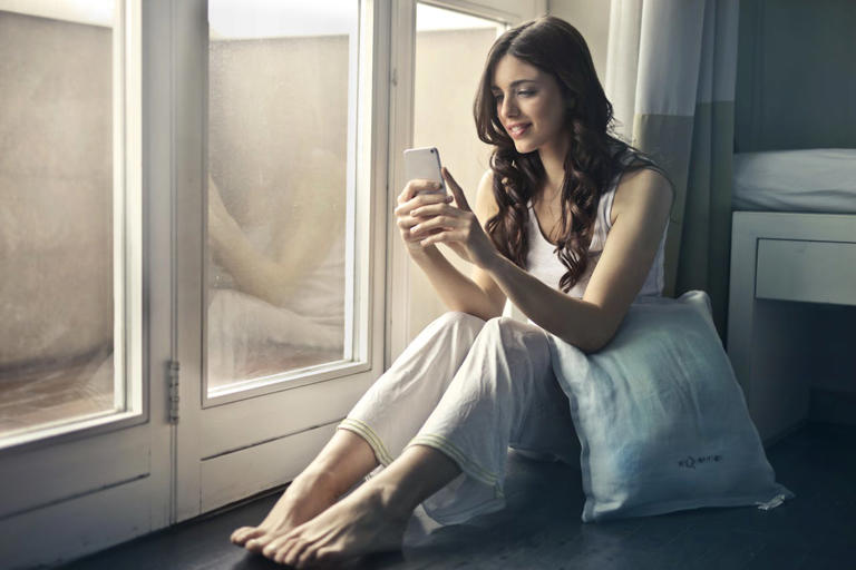 woman looking at phone in front of a window