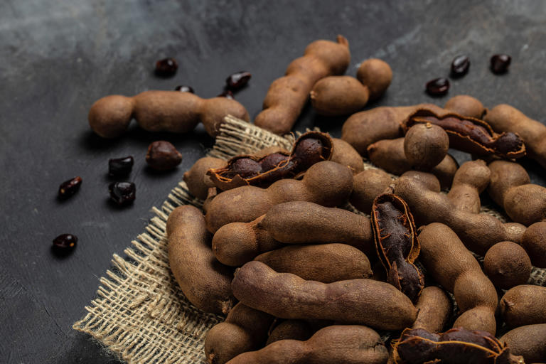Tropical fruits, Tamarindo beans in shell on a brown butchers block on a dark background, healthy fruit. banner, menu, recipe place for text, top view.