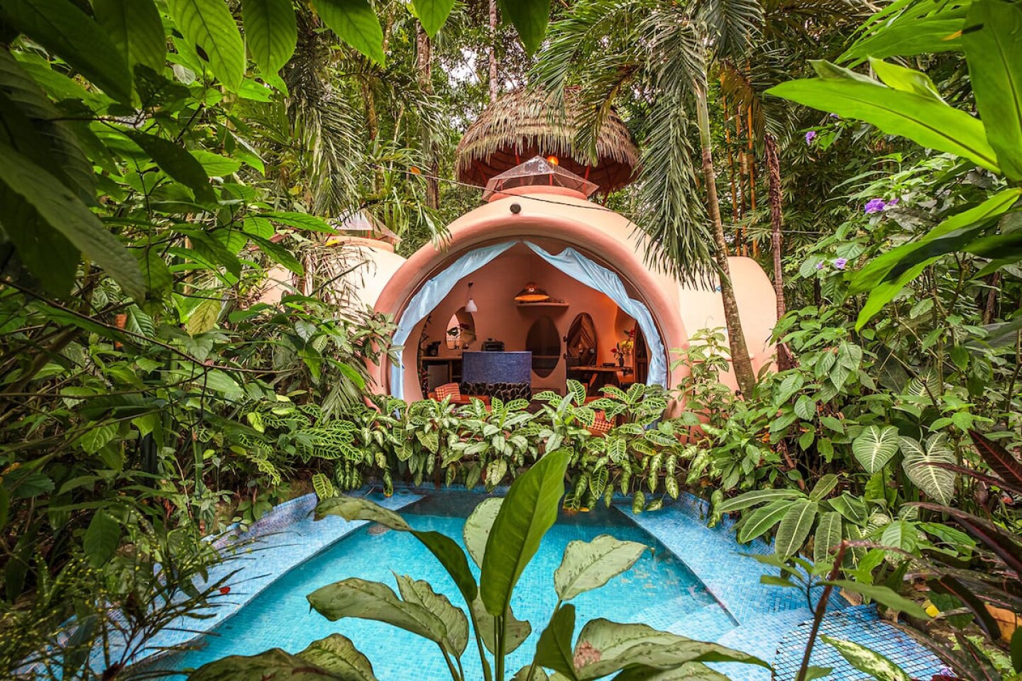 <a>The enormous round window in this whimsical house looks out to the lush, plant-surrounded pool.</a>