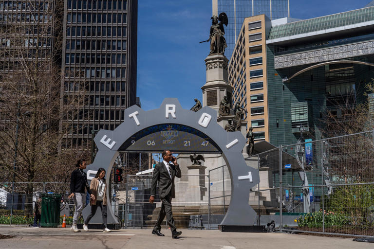 People walk past the countdown clock as work continues on the setup for the upcoming NFL Draft near Campus Martius in downtown Detroit on Tuesday, April 16, 2024.