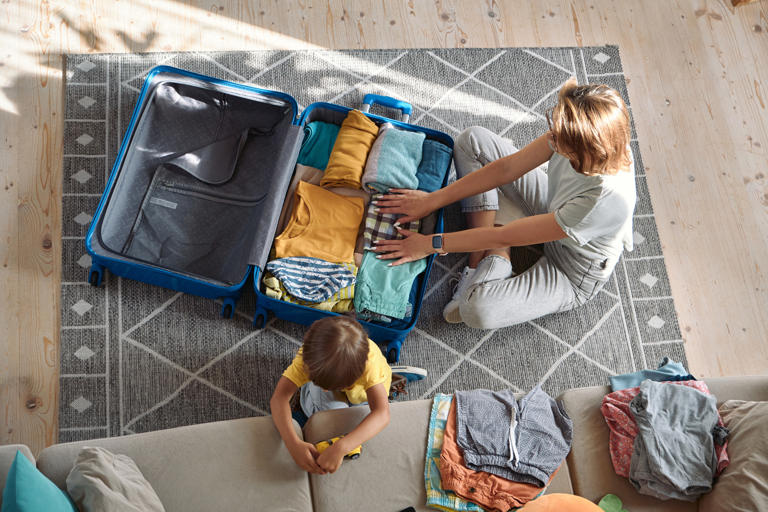 A stock photo shows a mom packing a suitcase. Travelling with kids can be hard, but planning can help.
