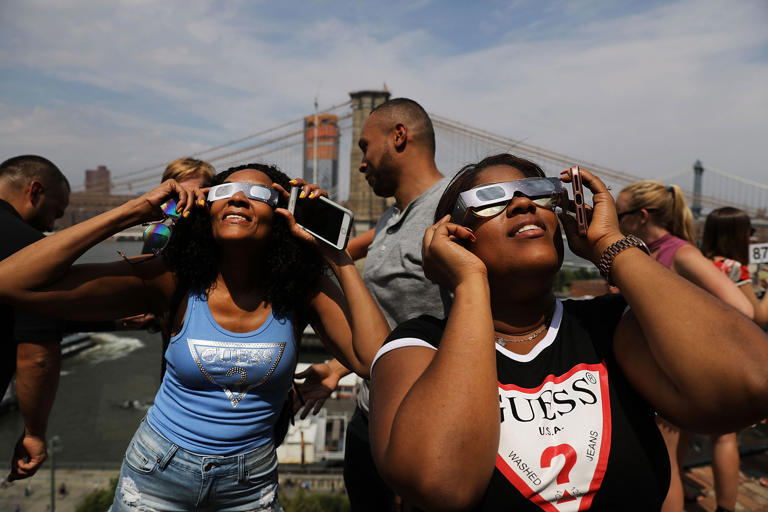 People watch a partial solar eclipse from the roof deck at the 1 Hotel Brooklyn Bridge in New York City, on August 21, 2017.