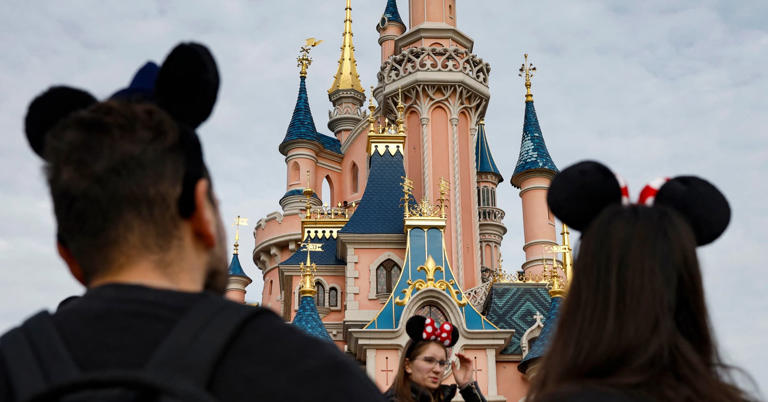Visitors wearing emblematic Mickey Mouse and Minnie Mouse ears walk in front of the Sleeping Beauty-inspired castle at Disneyland Paris, Oct. 16, 2023.
