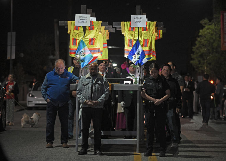 Esteban Conce De La Cruz, left, Baltimore Police officer Ayala and others stand in prayer before carrying the memorial bearing crosses, vests, hardhats and names of the six men who died in the Key Bridge collapse. Hundreds attend a bilingual prayer service held by The Archdiocese of Baltimore at the Sacred Heart of Jesus Christ that was followed by the candlelight prayer walk.