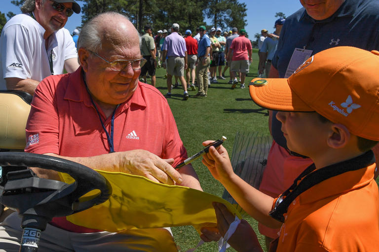 CBS broadcaster Verne Lundquist autographs a Masters flag for a fan at Augusta National GC.