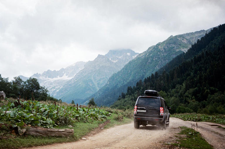 Check out this list of 10 of the Best Podcasts for Road Trips. Pictured: van driving in the mountains.