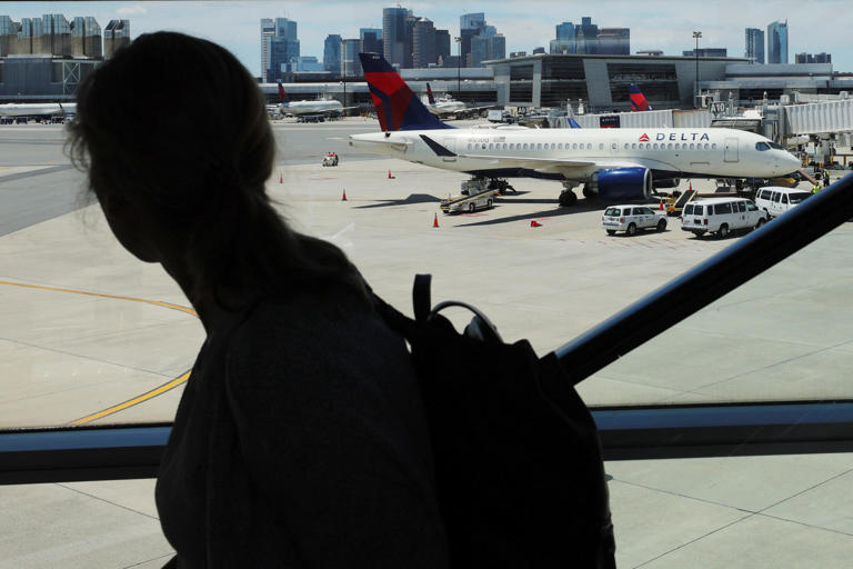 A traveler passes a Delta Airlines plane in Logan Airport at the start of the long July 4th holiday weekend in Boston, Massachusetts, U.S., June 30, 2022. REUTERS/Brian Snyder