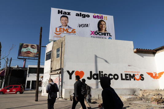 Peatones caminan frente a un anuncio que promueve el voto por Lemus y Gálvez en el periférico de la Zona Metropolitana de Guadalajara.