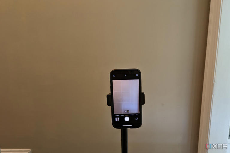 An iPhone on a tripod in front of a beige wall.