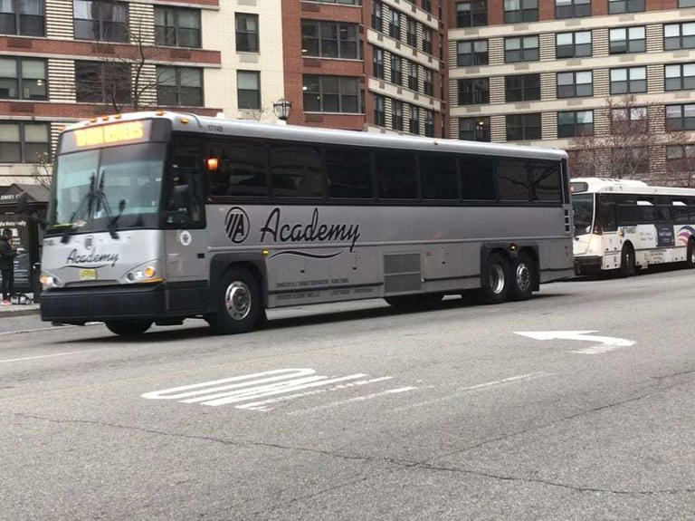 An Academy bus passes the Grove Street PATH station in Jersey City. Academy was awarded its first contract after making a settlement with the state over charges it defrauded NJ Transit. That agreement requires monitoring of company performance during this contract.