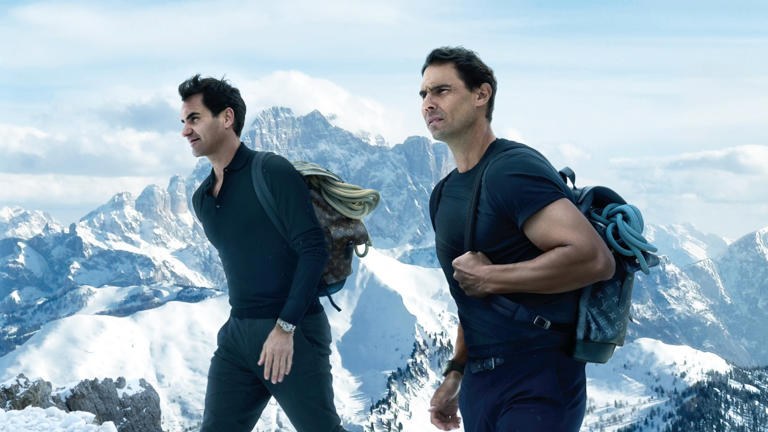 Two men in black striding through a snowy mountainscape carrying Louis Vuitton luggage on their backs