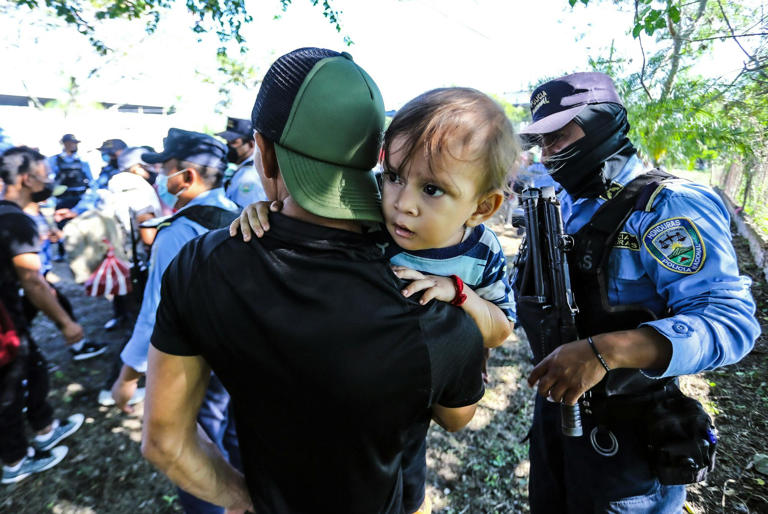 A man with a child shows his identification to police officers at a checkpoint in Honduras as migrants attempt to reach the U.S.