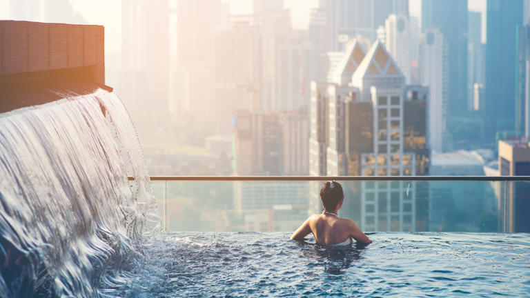 Asian travel. young woman enjoying the city view from roof top swimming pool.