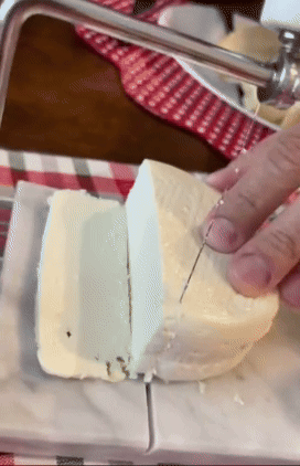 reviewer using the white marble based cheese slicer to wire cut through soft cheese
