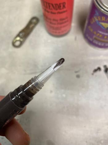 Person holding a pen with leaking ink cartridge, with blurred tools and containers in the background
