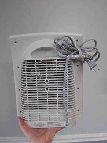 reviewer holding their space heater showing the cord bundler holding the space heater's cord neatly to the back of the machine