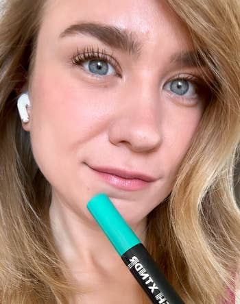 Close-up of a reviewer holding a mascara tube with fully done lashes
