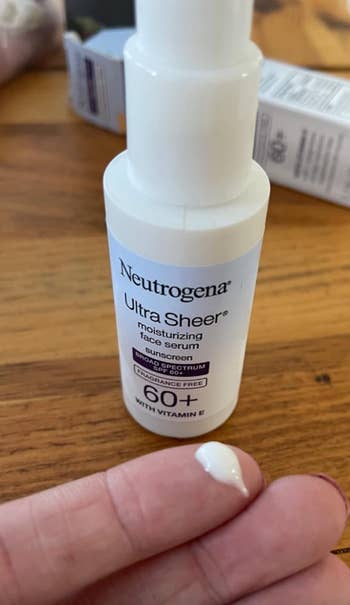 Hand holding a bottle of Neutrogena Ultra Sheer face serum with SPF 60+