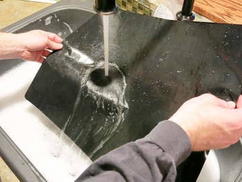 someone washing the oven liners in a sink